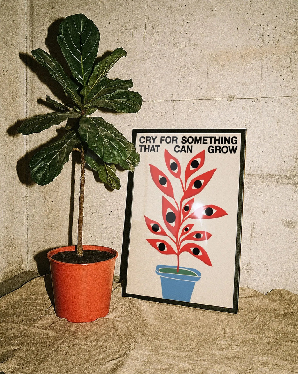 Stampa artistica moderna con pianta rossa con occhi e scritta “Cry for something that can grow”, poster design contemporaneo accanto a pianta verde in vaso su sfondo minimal